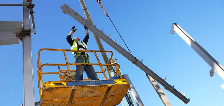 Trabajador construyendo una estructura de dos pisos con diversas piezas de acero