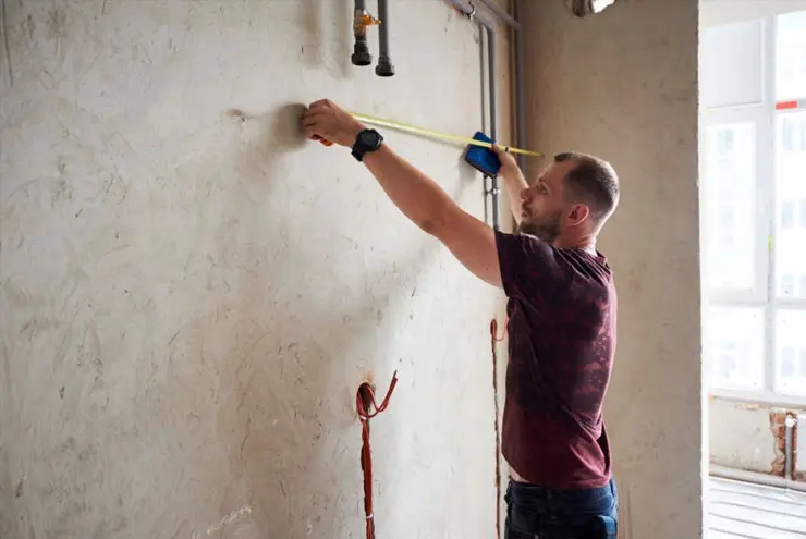 Persona midiendo la pared de su casa para calcular los metros cuadrados