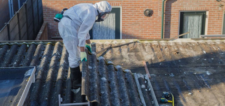 Persona con mascarilla quitando lámina de asbesto de un techo