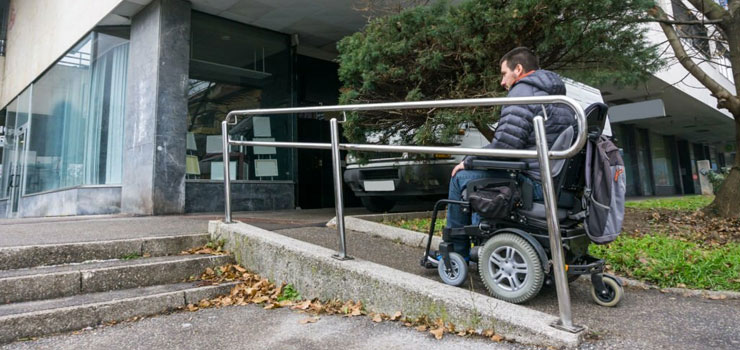 Hombre subiendo rampa para discapacitados con barandilla en silla de ruedas