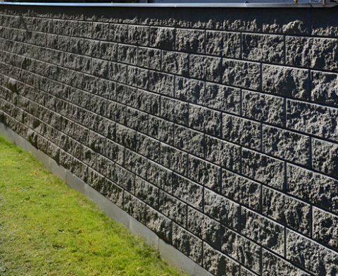 Barda de hormigón con bloques texturizados, formando un alto muro divisorio