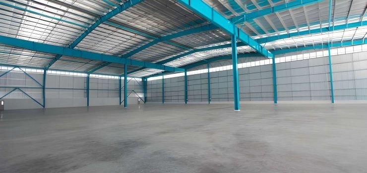 Interior vacío de una nave industrial metálica con armazón azul y cubierta blanca