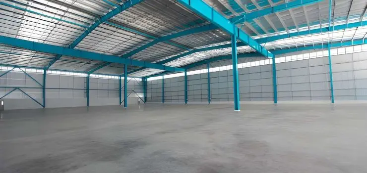 Interior vacío de una nave industrial metálica con armazón azul y cubierta blanca